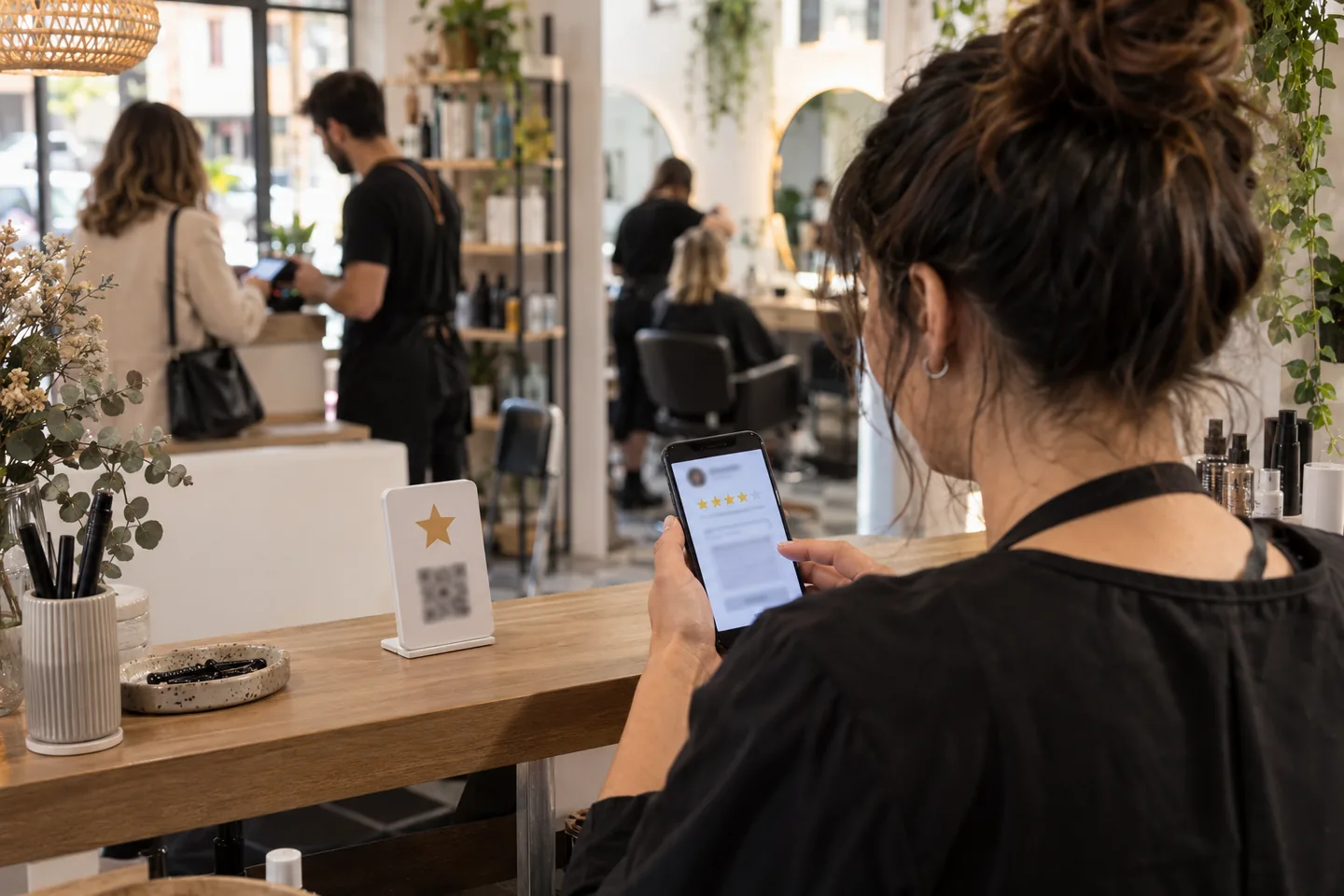 Dueña de una peluquería revisando en el móvil la respuesta a una reseña, con un soporte con código QR para opiniones en el mostrador